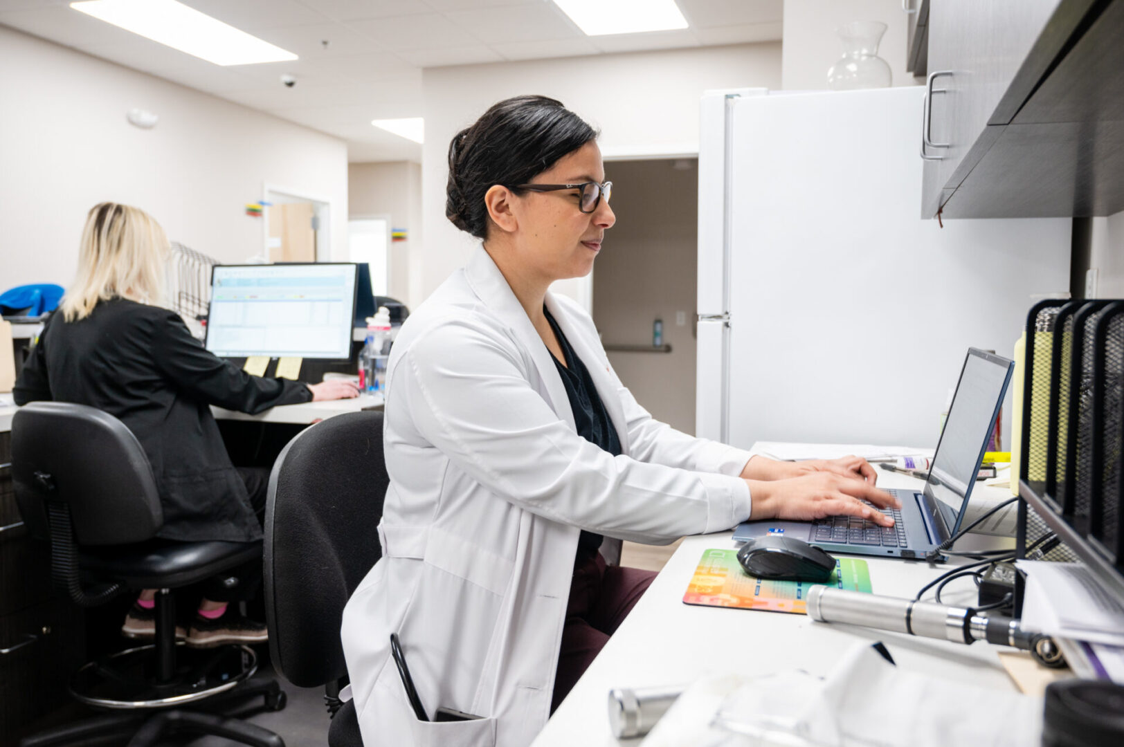 A woman in glasses and white lab coat using a computer.