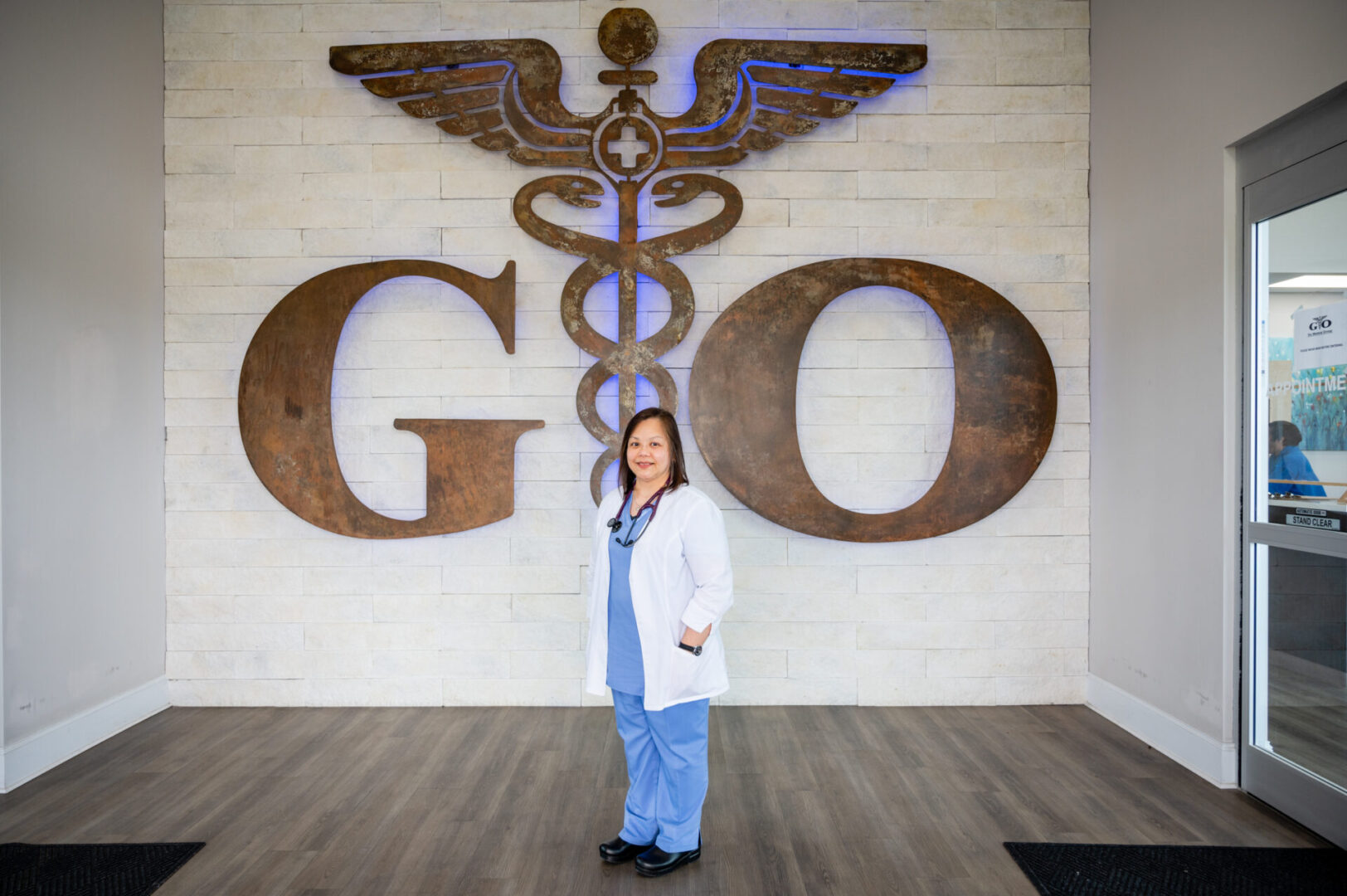 A woman in scrubs standing in front of a large sign.